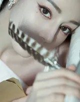 她倚靠墙面眼眸低垂，斜裁裙摆勾勒出修长身姿，静谧中散发迷人气息