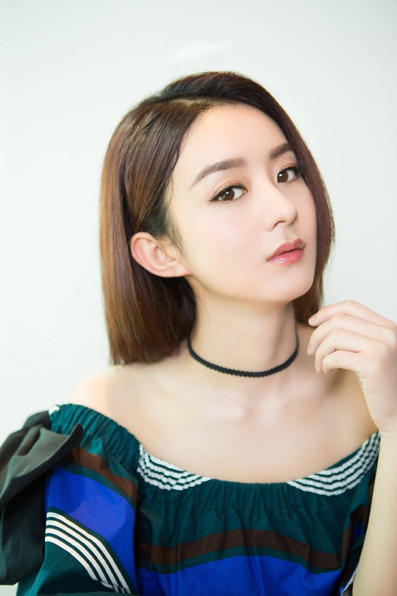 赵丽颖低头含笑，手微微轻触脸颊，身着带有细腻纹理的服装，整体画面充满羞涩而甜蜜的少女感。